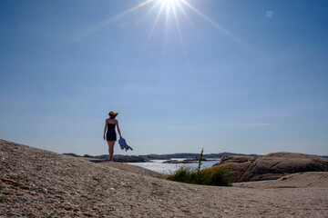 Sun shining over teenage girl walking alone along rocky shore