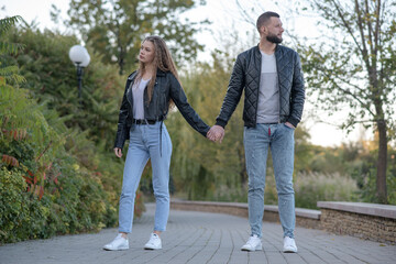 Attractive and stylish guy and girl dressed in autumn casual style are walking in the autumn park.