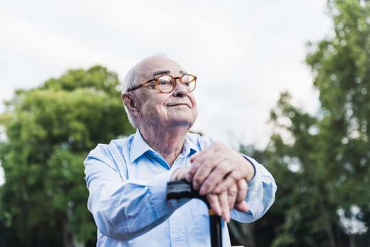 Portrait of senior man in a park leaning on his walking stick