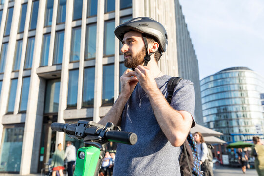 Man using e-scooter in Berlin, fastening safety helmet, Germany