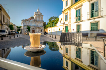 Coffee with milk called galao with landmark of Belmarco mansion in the background, Faro, Portugal