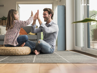 Young man and little girl sitting at home, giving high five