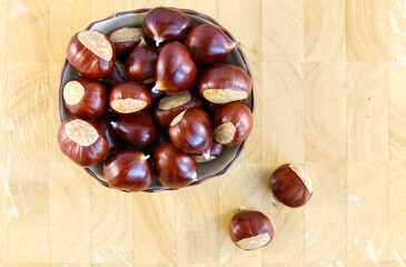A bowlful of fresh, raw sweet chestnuts on a wooden chopping board