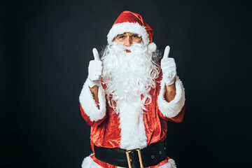 Man dressed as Santa Claus with thumbs up, on black background. Christmas concept, Santa Claus, gifts, celebration.