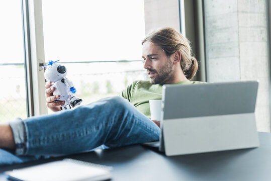 Young businessman sitting at desk in office holding robot