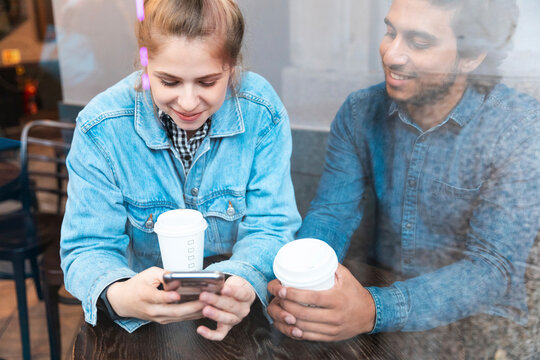 Young woman using smartphone in a coffee shop while her boyfriend watching her