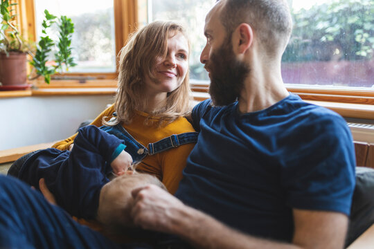 Woman on the sofa breastfeeding her little son and sharing time with her husband