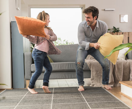 Young man and little girl having a pillow fight in the living room