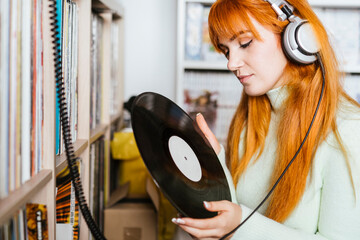 Redhead woman with headphones listening music while holding record at store