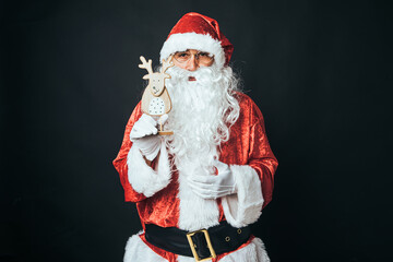 Man dressed as Santa Claus holding the figure of a wooden reindeer, on black background. Christmas concept, Santa Claus, gifts, celebration.
