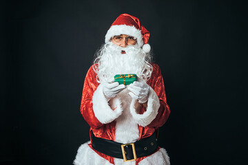 Man dressed as Santa Claus holding a parcel wrapped with wrapping paper, on black background. Christmas concept, Santa Claus, gifts, celebration.
