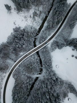 Aerial view of asphalt road stretching over river Ach flowing through snow-covered forest