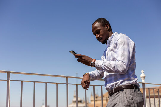 Male entrepreneur using smartphone while leaning on railing against clear blue sky