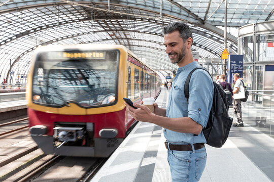 Smiling businessman at the station waiting for the train looking at the smartphone, Berlin, Germany