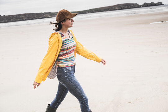 Young woman wearing yellow rain jacket at the beach, Bretagne, France
