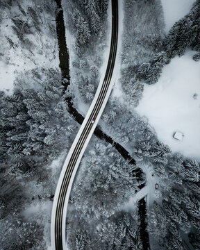 Aerial view of asphalt road stretching over river Ach flowing through snow-covered forest