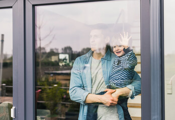 Father holding laughing son, looking out of window