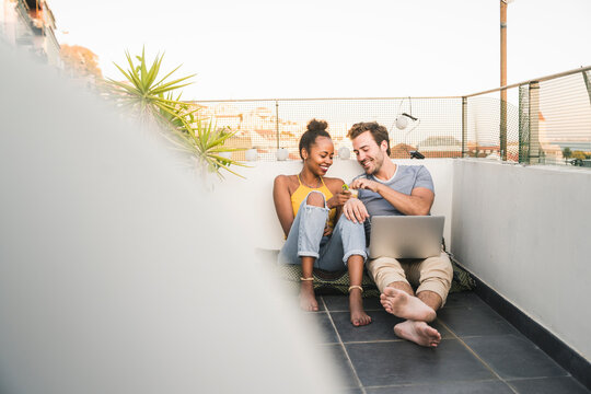 Young couple with laptop sitting on rooftop in the evening