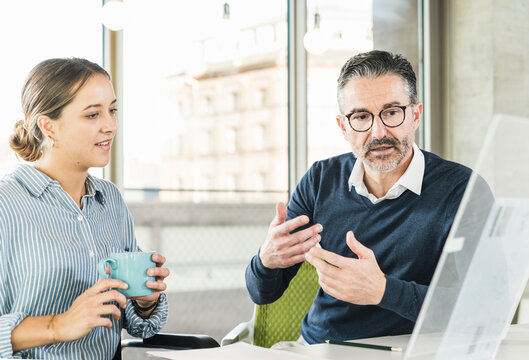 Mature businessman and young businesswoman talking at desk in office