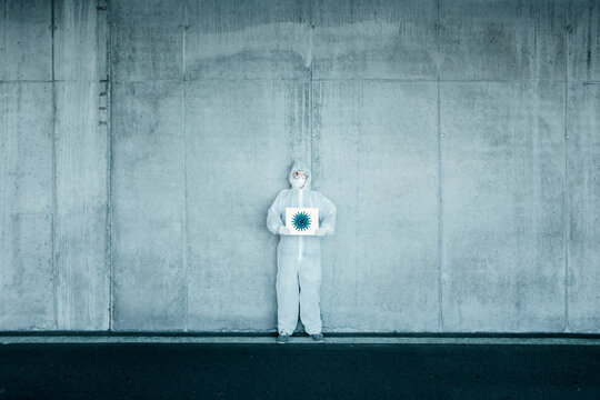 Man wearing protective clothing holding sign with a depiction of a virus