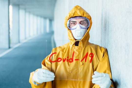 Portrait of man wearing protective clothing holding 'Covid 19' sign