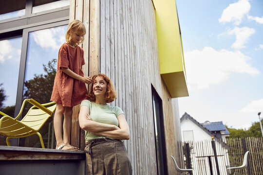 Girl tying mother's hair while standing outside tiny house