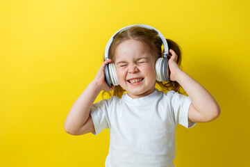 portrait of a cute cheerful little girl listening to music with white headphones. audiobooks, audio lessons. concept of education. photo studio, yellow background, text space. High quality photo