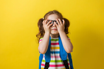 portrait of a girl with glasses and a striped T-shirt with a school backpack on a yellow background. joyful child is in a hurry to go to school. concept of education. photo studio, space for text. 