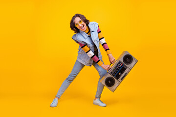 Fototapeta premium Full size photo of crazy white hairdo old lady hold boom box dance wear eyewear sweater vest jeans shoes isolated on yellow background