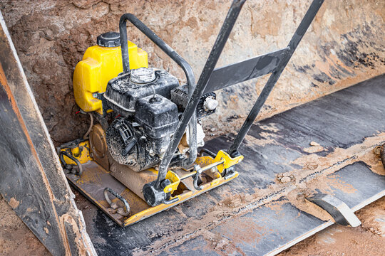 Vibratory rammer with vibrating plate on a construction site. Compaction of the soil before laying paving slabs. Close-up.