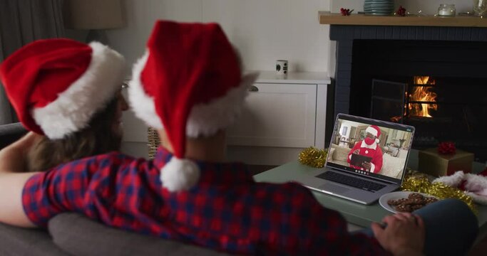 Caucasian couple on laptop video call with santa claus in face mask at christmas time