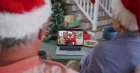 Happy senior caucasian couple on video call on laptop with santa in face mask at christmas time - Powered by Adobe