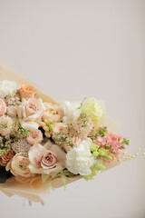 Young woman holding big delicate bouquet flowers in beige color wrapped in paper.