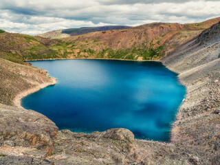 Fototapeta na wymiar Blue mountain lake in the caldera. Mountain range against a cloudy sky. Caldera of an extinct volcano is surrounded by a mountain range. In the valley there is a blue lake with steep rocky shores.