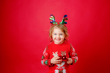 Cute little girl in a red sweater with deer horns on a red background smiling, Christmas, New Year