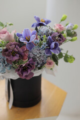 Floral bunch in round grey box. Fresh delicate bouquet of beautiful mixed flowers in light room. The work of a professional florist. 