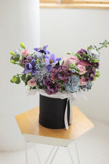 Floral bunch in round grey box. Fresh delicate bouquet of beautiful mixed flowers in light room. The work of a professional florist. 