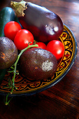 Mixed raw vegetables on a plate: cherry tomatoes, avocados, zucchini and eggplant