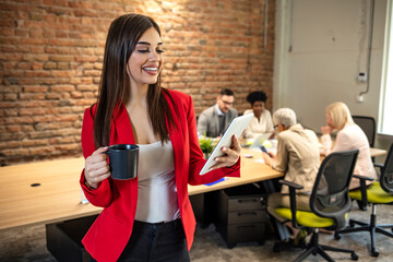 Shot of young business woman entrepreneur looking at camera in the office. In the background, her colleagues working. Beautiful business woman Texting in the coffee break