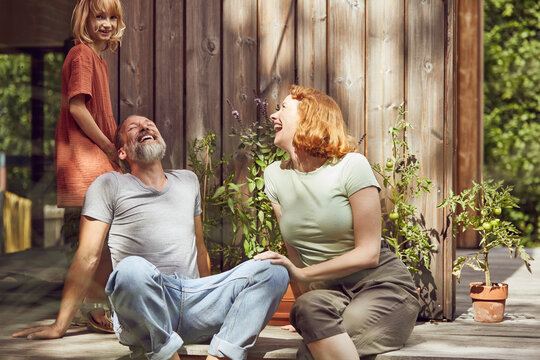 Girl standing by cheerful parents laughing while sitting outside tiny house