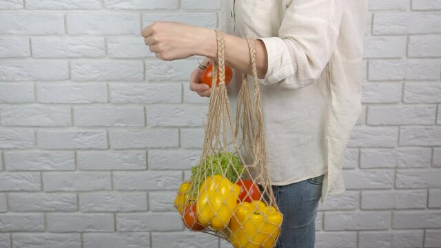 Vegetables vitamines in a bag. A woman use an eco net and puts vegetables in it in the kitchen.