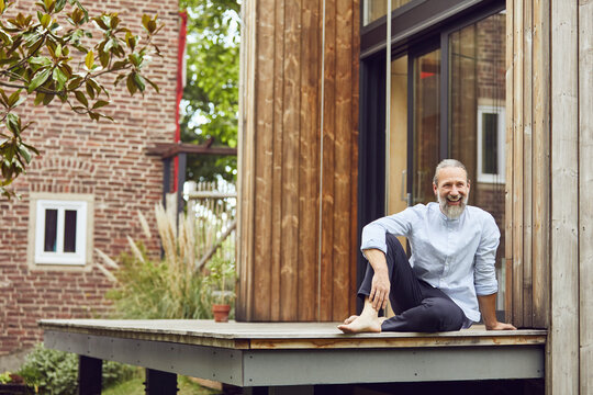 Happy Bearded Man Sitting On Hardwood Floor Outside Tiny House