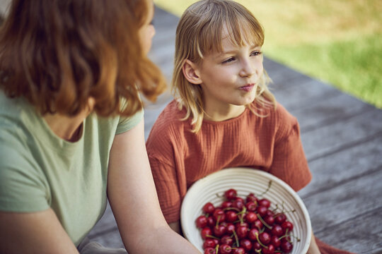 Close-up of mother and daughter eating cherries while sitting in yard