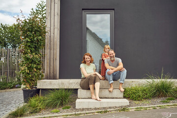Smiling parents with girl sitting on steps outside tiny house