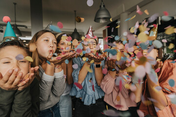Playful friends blowing confetti while enjoying birthday party at home
