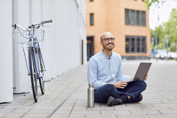 Smiling mid adult man using laptop while sitting on street