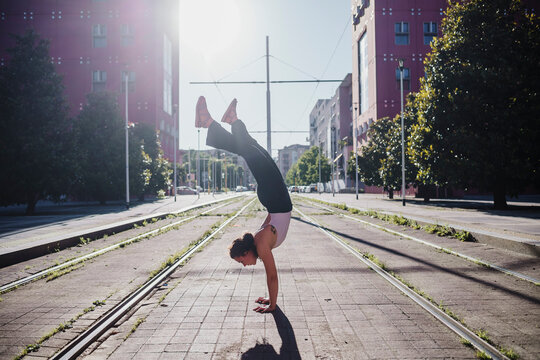 Young woman performing handstand on tramway in city during sunny day