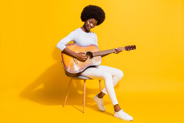 Full size photo of optimistic short hair lady play guitar wear white pullover trousers sneakers isolated on yellow background