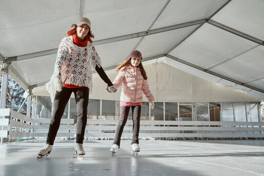 Mother holding hand of her daughter , while ice skating