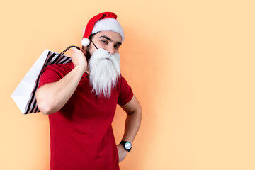 Fototapeta premium Young man with Santa Claus hat and white beard, with shopping bags. Front view.